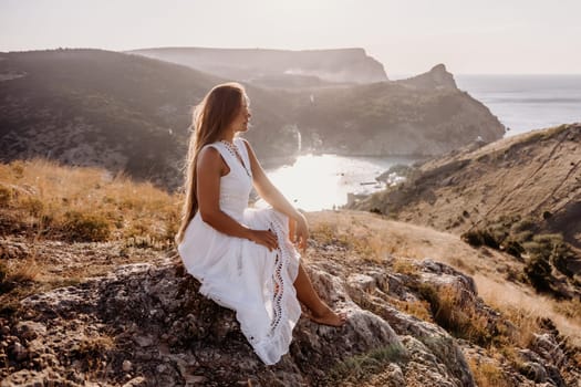 A woman in a white dress sits on a rock overlooking a body of water. The scene is serene and peaceful, with the woman enjoying the view and the calmness of the surroundings