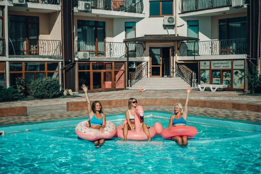 Three women are sitting on inflatable floats in a pool. Scene is lighthearted and fun