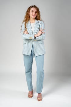 Young woman with curly hair in blue jacket posing on gray background close up