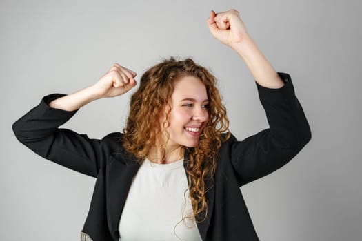 Joyful Young Woman Dancing Alone in Light-Colored Casual Attire Against a Grey Background close up