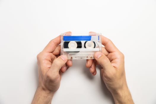 White and blue cassette in male hands on a white background, top view. Mock-up for an inscription on a magnetic cassette, an object of old luxury.