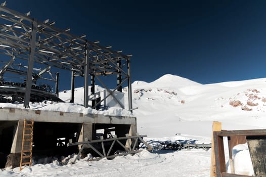 A cable car station under construction high in the mountains in winter. Focus on a close-up of a thick cable car cable covered with snow.