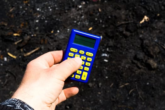 Blue calculator in dark soil, burnt ground after a fire