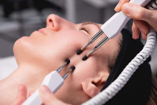 Close-up of a woman receiving an electric neck massage with equipment in a beauty salon. Used for therapy with a multifunctional electro massage device.