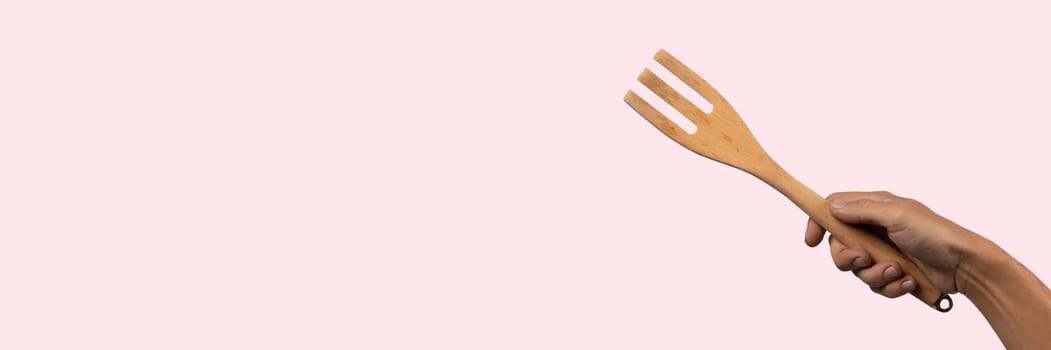 Hand holding wooden fork on pink background. High quality photo.