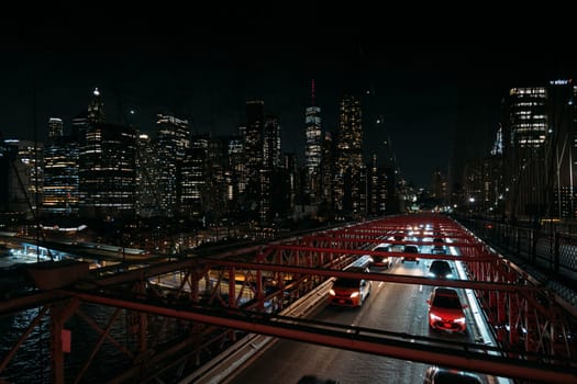 Nighttime scene of New York City skyline with bright city lights and heavy traffic on an illuminated bridge. The city's iconic skyscrapers and urban environment under a dark sky prominently featured.