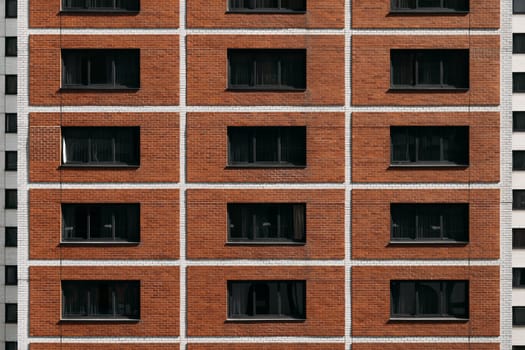 The symmetrical facade of a modern brick apartment building features rows of evenly spaced dark windows. The structure exhibits a blend of contemporary and traditional architectural elements.