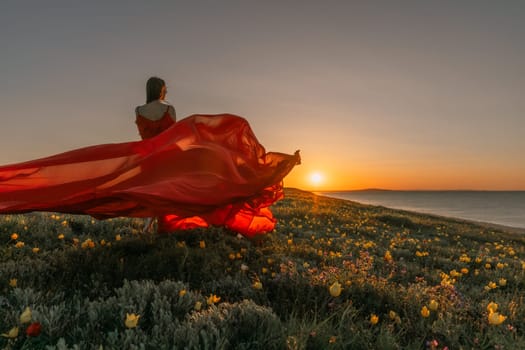 A woman in a red dress is standing in a field with the sun setting behind her. She is reaching up with her arms outstretched, as if she is trying to catch the sun. The scene is serene and peaceful