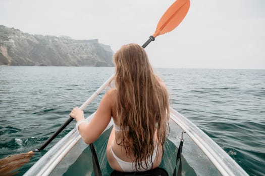 Woman in kayak back view. Happy young woman with long hair floating in transparent kayak on the crystal clear sea. Summer holiday vacation and cheerful female people having fun on the boat.