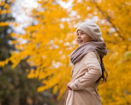 Happy caucasian girl in a beige coat and beret walks in the park in autumn