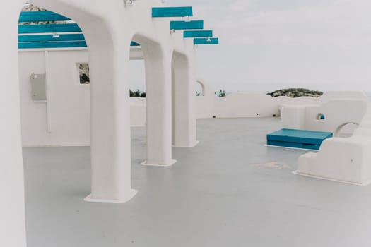 A white building with blue accents, and the blue accents are on the pillars. The building is located near the ocean, and the blue accents give it a unique and interesting appearance