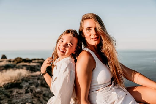 Close up portrait of mom and her teenage daughter hugging and smiling together over sunset sea view. Beautiful woman relaxing with her child.