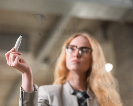 Caucasian woman with glasses writes text in English on a glass wall