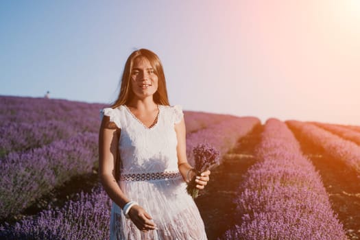 Close up portrait of young beautiful woman in a white dress and a hat is walking in the lavender field and smelling lavender bouquet.