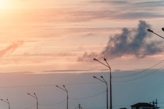 A sky with a few clouds and a street with a few street lights. The sky is a mix of blue and orange