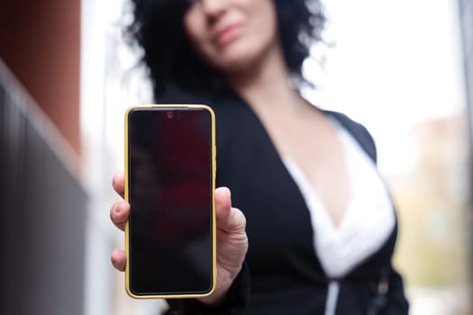 woman shows a smartphone with an empty screen for advertising or presentation, look at camera., smiling. Gadget Concept