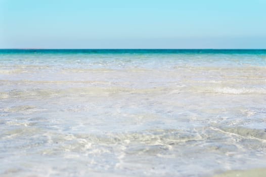 Bumpy tropical sandy beach with blurry transparent ocean and blue sky.
