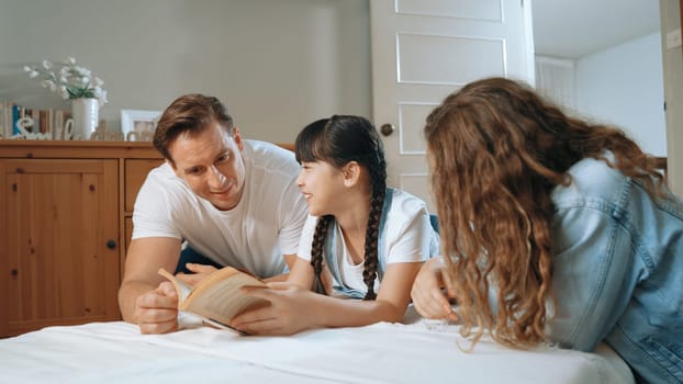 Bedtime story with childhood storytelling, mom and dad reading a fantasy book together to their little young girl in cozy and comfortable bedroom. Modern family happy time. Synchronos