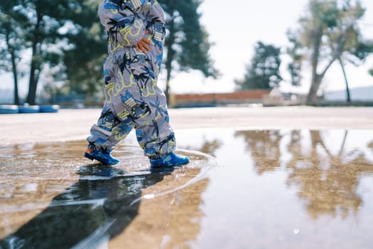 Small child in overalls walks through a puddle. Cropped. Faceless. High quality photo