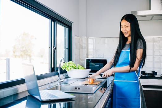 In the kitchen a smiling woman stands engrossed in cooking while using her laptop for tutorials. Emphasizing the joy of technology in culinary exploration and meal planning.