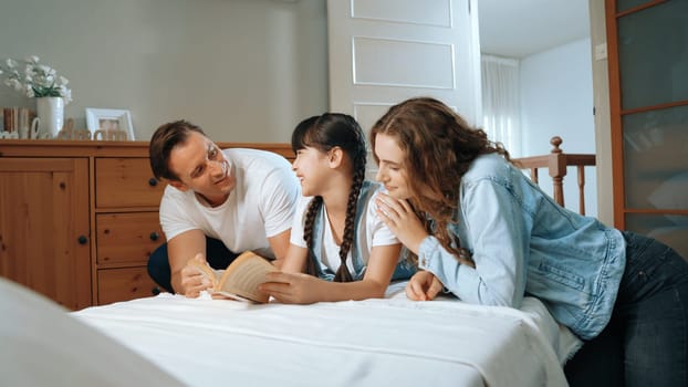 Bedtime story with childhood storytelling, mom and dad reading a fantasy book together to their little young girl in cozy and comfortable bedroom. Modern family happy time. Synchronos