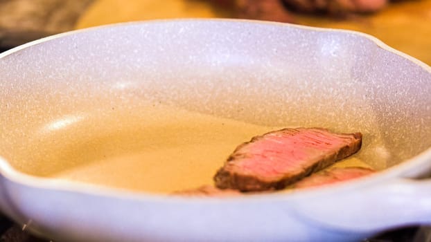 Tongs turning succulent medium-rare steak strips in a speckled ceramic skillet.