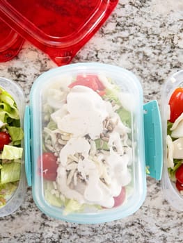 Containers filled with salad and dressing, prepared for convenient lunchtime meal prep.