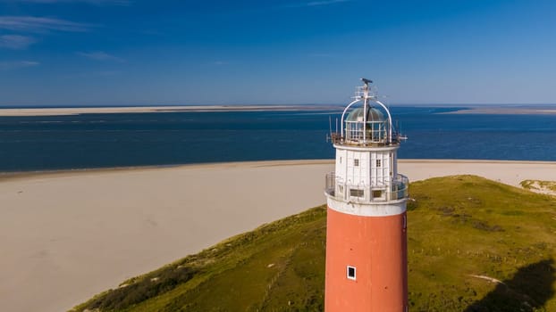 An aerial perspective of a majestic lighthouse standing tall on a sandy beach, its beacon shining brightly against the vast ocean.The iconic red lighthouse of Texel Netherlands
