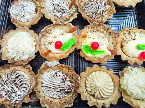 Assortment of Cream Topped Tarts in Display Case. Rows of freshly baked tarts topped with cream and garnishes