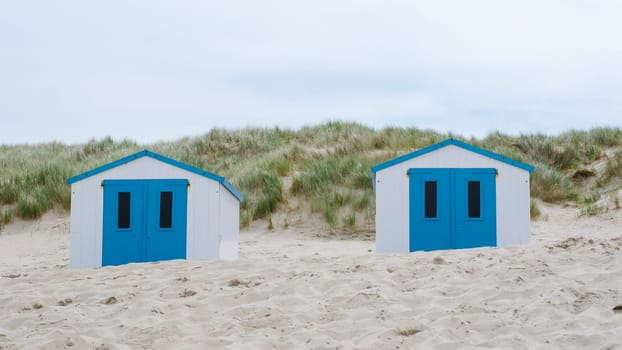 Two charming beach huts with vibrant blue doors stand out amidst the sandy shores of Texel, inviting visitors to relax and enjoy the seaside views. De Koog beach Texel