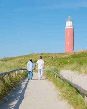 Two individuals strolling along a path near a charming lighthouse in Texel, Netherlands, enjoying the serene coastal scenery. a couple of men and women at The iconic red lighthouse of Texel Netherlands