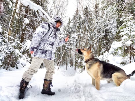 Adult girl or mature lady with shepherd dog in winter nature landscape in forest. Middle aged woman training big shepherd dog in cold day. Friendship, love, communication, fun, hugs