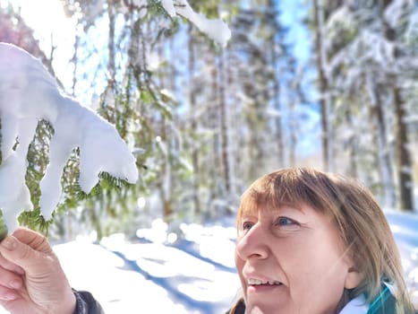 A cheerful middle aged woman in a winter coat taking selfie on nature outdoors in sunny day with blue sky