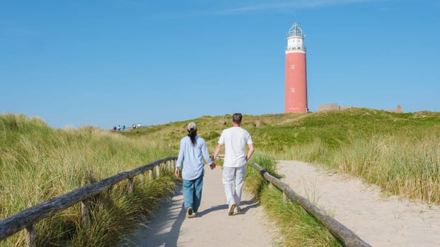 A romantic couple strolls along a scenic path, hand in hand, with a majestic lighthouse in the background, casting a warm glow over the Texel Netherlands coast.
