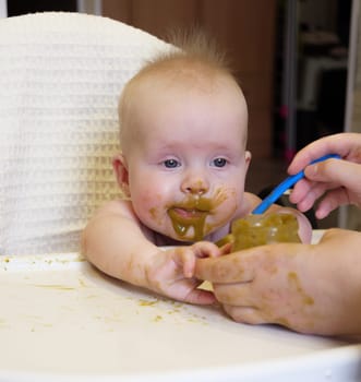 Mom feeding little boy with broccoli puree. Child at the age of six months eats broccoli while sitting on a baby chair.