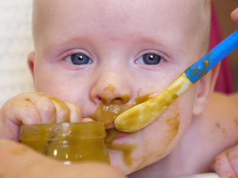 Mom feeding little boy with broccoli puree. Child at the age of six months eats broccoli while sitting on a baby chair.