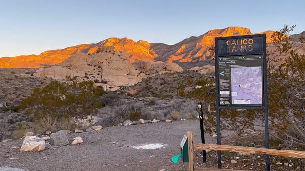 The Calico Tanks Trailhead at sunrise with a glowing mountain view. Trailhead sign and map - Red Rock Canyon National Conservation Area, Nevada, USA
