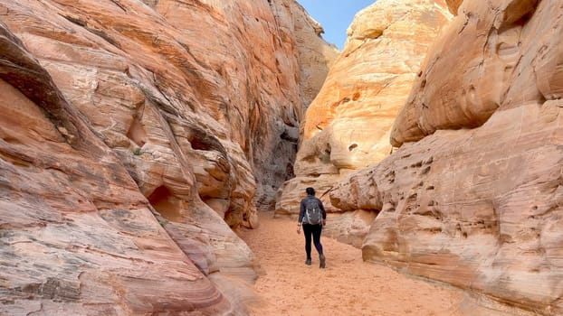Female hiker walking into the narrow, pink and perfectly carved by erosion walls of the Kaolin Slot Canyon - Valley of Fire State Park, Nevada, USA