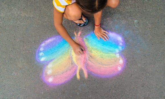 A child draws a butterfly on the asphalt with chalk. Selective focus. Kid.