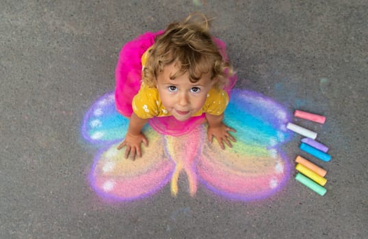 A child draws a butterfly on the asphalt with chalk. Selective focus. Kid.