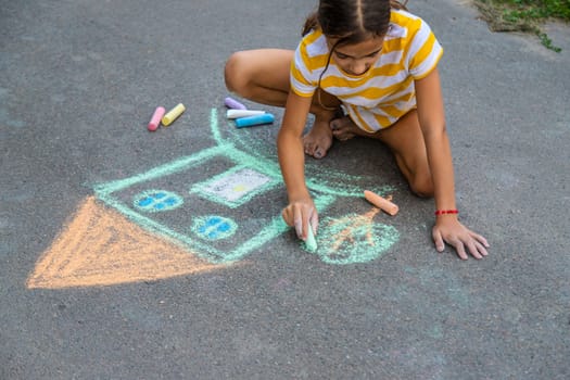 A child draws a house on the asphalt with chalk. Selective focus. Kid.