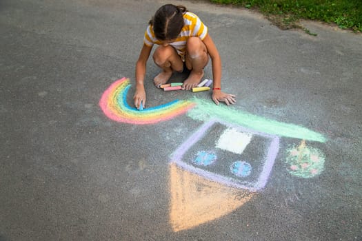 A child draws a house and a rainbow on the asphalt with chalk. Selective focus. Kid.