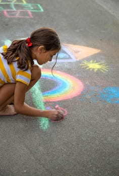 A child draws a house and a rainbow on the asphalt with chalk. Selective focus. Kid.