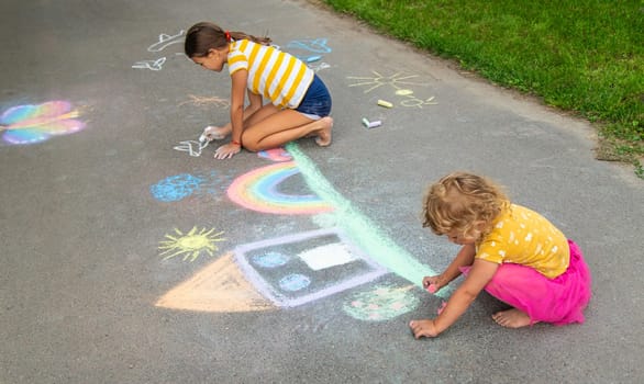 A child draws a house and a rainbow on the asphalt with chalk. Selective focus. Kid.