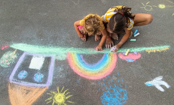 A child draws a house and a rainbow on the asphalt with chalk. Selective focus. Kid.