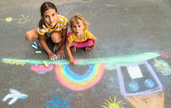 A child draws a house and a rainbow on the asphalt with chalk. Selective focus. Kid.