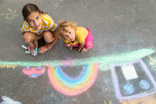 A child draws a house and a rainbow on the asphalt with chalk. Selective focus. Kid.