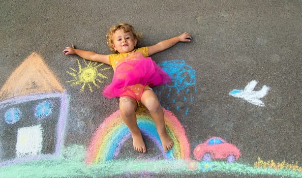 A child draws a house and a rainbow on the asphalt with chalk. Selective focus. Kid.