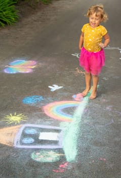 A child draws a house and a rainbow on the asphalt with chalk. Selective focus. Kid.