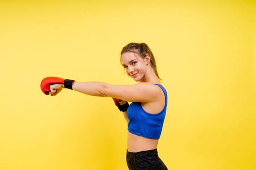 Woman boxer in gloves training on a grey and yellow background studio